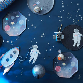 A space-themed table setting featuring plates with planet designs, astronaut motifs, a rocket ship, and a cup adorned with stars, set against a starry tablecloth, perfect for a cosmic celebration.