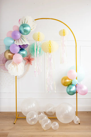 An arch adorned with My Mind's Eye's Honeycomb Jellyfish Set, colorful balloons, and whimsical party decorations, set against a neutral wall and wooden floor.