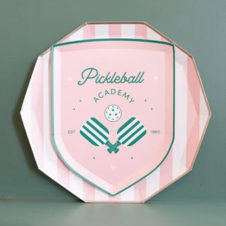 A decorative octagonal plaque with a pastel pink and mint design, featuring the emblem of "pickleball academy" with pickleball paddles and a ball, established in 1965, crafted from Bonjour Fête's Le Pickleball Small Plates.