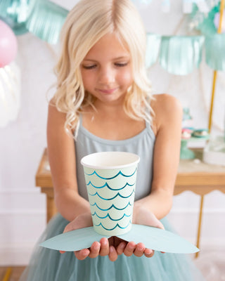 Young girl holding a My Mind's Eye Mermaid Tail Paper Party Cup at a party, surrounded by balloons and decorations.
