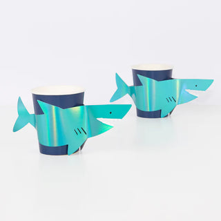 Two holographic foil Meri Meri shark cups on a white surface.