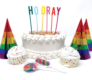 A colorful rainbow cake with Party Partners' Hooray Acrylic Cake Topper and cupcakes.
