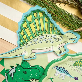 Colorful cartoon dinosaur illustrations displayed on elegant Sophistiplate Dinosaur Salad Plates alongside pine foliage, showcasing a vibrant spinosaurus and a peek of other dinosaur designs.
