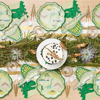 A festive dinosaur-themed table setting features elegant Sophistiplate Dinosaur Salad Plates, gold cutlery, a centerpiece cake with a dinosaur topper, and decorative greenery, creating a playful and imaginative dining atmosphere.