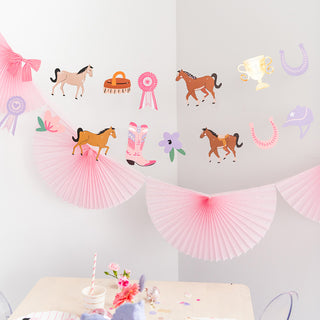A festive room with horse-themed decor, including wall stickers and pink paper fans, set above a table with party remnants, possibly after a child's birthday celebration.