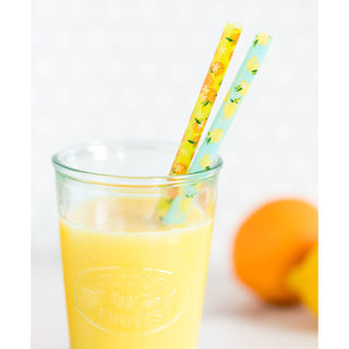 A refreshing glass of orange juice with two colorful patterned straws, accompanied by a whole orange in the soft-focused background suggesting a fresh, homemade beverage.