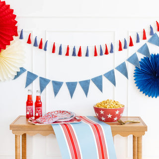 Decorated table with popcorn, soda, plates, and napkins. Red, white, and blue tassels and fans hang on the wall.