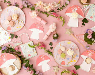 A whimsical tea party setup with a pastel pink theme, featuring mushroom plates, floral decorations, macarons, and enchanting garden elements, creating a magical fairy-tale atmosphere.