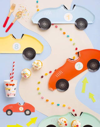 A creative race car-themed party setup with colorful paper car cutouts, number decals, playful utensils, and a track adorned with sweets and cupcakes, evoking a festive and fun atmosphere for children.