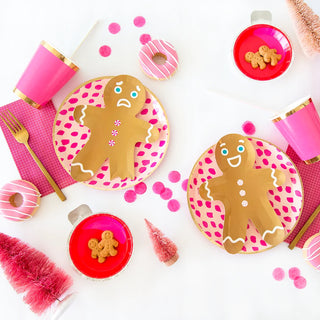 A vibrant children's party setup with a theme featuring gingerbread men plates, assorted sweets, pink cups, and playful decorations contrasting against a white background.