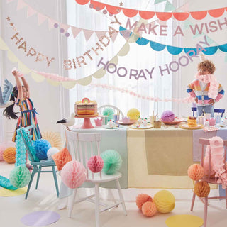A colorful birthday party scene with joyful children, a cake on the table, and decorations including banners, balloons, and hanging paper ornaments.