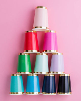 A vibrant pyramid of colorful paper cups with gold trim arranged on a pink background, showcasing a mix of red, pink, green, blue, and black shades.