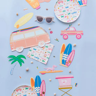 Beach-themed items on a light blue background, including sunglasses, a toy van, surfboards, a palm tree, a small car, and paper plates with colorful patterns.