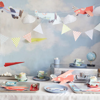 A playful, aviation-themed kids' party setup with paper airplane decorations, colorful tableware featuring planes, cloud motifs, and a whimsical sky backdrop, evoking a sense of adventure and fun.