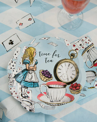 An alice in wonderland-themed tea party setting with an illustrated plate featuring alice, a pocket watch, and a cup, alongside playing card symbols, set on a blue and white checkered tablecloth with a refreshing drink in the background.