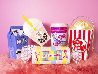 A vibrant collection of whimsical purses with designs mimicking a milk carton, bubble tea, popcorn, and a pencil case, playfully arranged against a pink backdrop, evoking a fun, youthful fashion statement.
