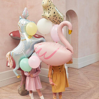 Two children stand amidst a collection of vibrant balloons, including a unicorn, leopard, and flamingo, their faces obscured by the balloons during a playful, festive celebration.