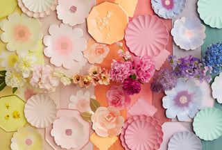 An array of pastel paper flowers and live blooms in soft pinks, blues, and yellows meticulously arranged on a multicolored backdrop, creating a visually soothing, pattern-rich tableau.
