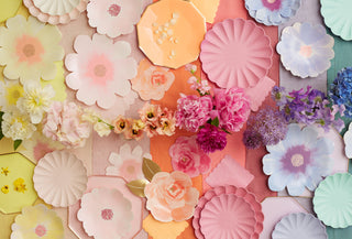 Assortment of colorful paper flowers and fresh blossoms laid out in a gradient, crafting a vibrant, spring-themed backdrop with a touch of whimsical charm.