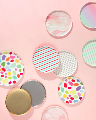 An assortment of colorful, patterned round lids casting soft shadows on a pastel pink background, showcasing a variety of designs including stripes, polka dots, and marbling.