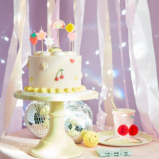 A whimsical birthday cake adorned with colorful toppers and pastel decorations sits on a pedestal, surrounded by cheerful party accessories, evoking a playful, festive atmosphere.