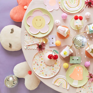 A cheerful, pastel-themed party setup with assorted plates, decorations, a disco ball, and thematic accessories laid out on a pink background, exuding a playful and whimsical vibe.