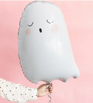 A person holds a cute ghost-shaped balloon with blushing cheeks and a sleepy expression, against a soft pink backdrop.