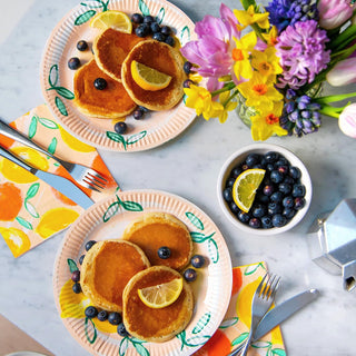 A cheerful breakfast table setup with plates of fluffy pancakes garnished with fresh blueberries and lemon wedges, accompanied by a side bowl of extra blueberries and a vibrant bouquet of spring flowers adding a pop of color to the scene.