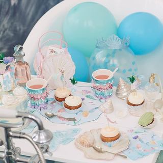 A whimsical mermaid-themed party setup with pastel cupcakes, iridescent tableware, delicate bottles, and matching balloons creating an enchanting underwater ambiance.