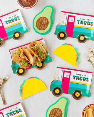 Playful taco holders designed as colorful food trucks, accompanied by vibrant avocado-themed plates, add a whimsical touch to a fun and festive meal setup.