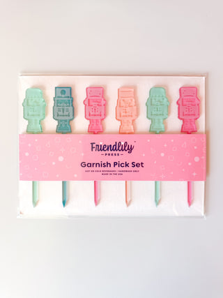 A festive Nutcracker Garnish Pick Set candy, featuring pink, blue, green, and yellow colors by Friendlily Press.