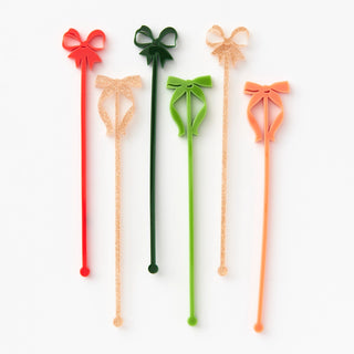 The Paper Source Acrylic Bow Drink Stirrers come in a set of five vibrant colors, featuring bow designs in red, green, and glitter. Arranged on a white background, these stirrers are ideal for adding a festive touch to holiday parties.