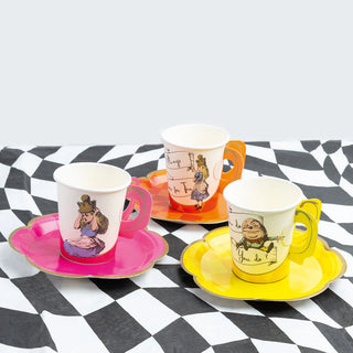 Three cups from the Alice in Wonderland Bright Tea Cup Set by Talking Tables, each adorned with illustrated characters and placed on matching flower-shaped paper saucers, sit on a black-and-white checkered surface—a charming addition to the Alice collection.