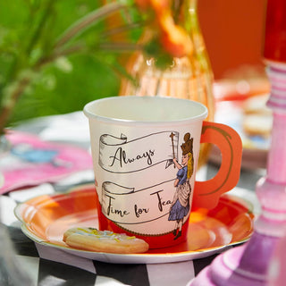 An Alice in Wonderland Bright Tea Cup from Talking Tables, adorned with "Always Time for Tea" and a Victorian-style illustration, sits on an orange plate next to a cookie, surrounded by the vibrant colors of the eclectic Alice collection.