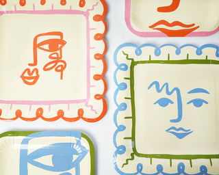 Art Party Dinner Plates by Pop! Party Supplies feature abstract, colorful face designs in orange, blue, green, and pink. Each plate showcases a distinct face and border pattern on a white background. Pair them with Picasso-inspired cups for an artistic flair at your next gathering.