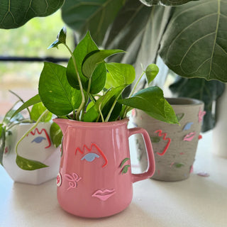 Colorful ceramic pots with abstract face designs hold green leafy plants, accented by **Art Party Puffy Stickers by Pop! Party Supplies**, with a pink pot prominently in the foreground and two other pots partially visible in the background.