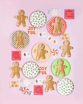 A festive holiday setup featuring gingerbread cookies, vibrant Gingerbread Man Plates by Jollity & Co, and cheerful holiday cards on a light pink background.