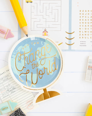 A Back To School Globe Paper Plate by My Mind’s Eye sits on a desk surrounded by school supplies, including a pencil, eraser, clipboard, and worksheets—perfect for a back to school party.