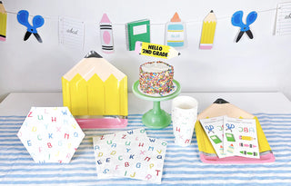 A back-to-school themed setup from Merrilulu features a cake on a green stand, various school supplies, alphabet-themed plates, and a "Hello 2nd Grade" sign, all arranged on a blue-striped tablecloth—perfect for classroom decoration. Enhance the look with the Merrilulu Back To School Garland for an extra festive touch.