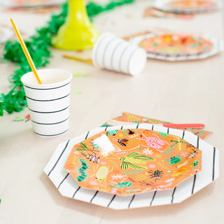 A table set featuring vibrant Backyard Bugs Small Plates by Daydream Society, paired with striped cups and disposable cutlery, all enhanced by a green garland decoration. Perfect for any bug enthusiast wanting to add a splash of color to their event.