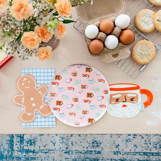 Create a festive kitchen ambiance with a gingerbread-shaped coaster, a stunning floral centerpiece, eggs in a carton, cookies cooling on the rack, and an intricately designed holiday plate next to the Baking Spirits Bright Santa Mug Large Napkins by Daydream Society—all elements that encapsulate the holiday cheer perfectly.