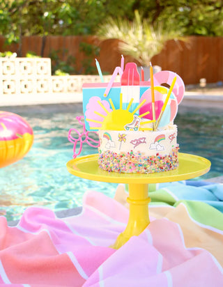 An kailo chic yellow Sun Acrylic Cake Topper sits on a table next to a pool.