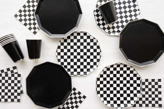 Black disposable plates and cups arranged on a white surface with Bonjour Fête's Black and White Signature Checker Large Napkins.