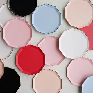 A variety of octagonal, faceted plates in different colors, including red, black, white, blue, pink, and beige Blanc White Premium Dinner Plates by Bonjour Fête with their elegant design are scattered on a light-colored surface.