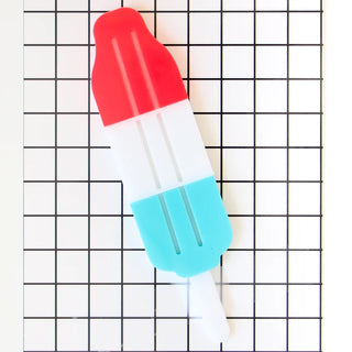 A Bomb Pop Acrylic Cake Topper adorned with a patriotic red, blue, and white design, perfect for a summer birthday celebration or bomb pop themed party by kailo chic.