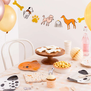 A joyful pet-themed party setup with Daydream Society Bow Wow Thingamajigs decorations, balloons, treats on a wooden stand, and themed tableware, creating a festive atmosphere for a celebration.