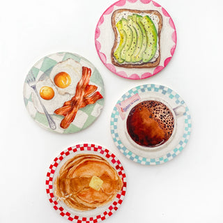 The "Breakfast Plates Coaster Set" by Cami Monet includes four watercolor coasters showcasing breakfast delights: avocado toast, eggs with bacon, a cup of coffee, and a stack of pancakes with butter. These coasters are perfect for adding a touch of brunch plate charm to your coffee table.