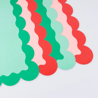 Meri Meri's Christmas Paper Placemats, featuring scalloped edges in red, green, and pink, are beautifully layered together to create a festive look reminiscent of classic holiday table settings.