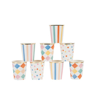 A pyramid formation of seven Meri Meri Colorful Pattern Cups, each featuring vibrant patterns of stripes, dots, and diamond shapes, arranged on a white surface against a plain background. These eco-friendly FSC mix paper cups add a playful touch to your decorative arrangements.