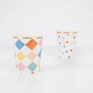 Two decorative Colorful Pattern Cups by Meri Meri with vibrant designs. The nearest cup showcases a pastel diamond pattern with a brushed effect, while the farther cup boasts playful polka dots on a white background. Crafted from FSC mix paper, they offer an eco-friendly choice.